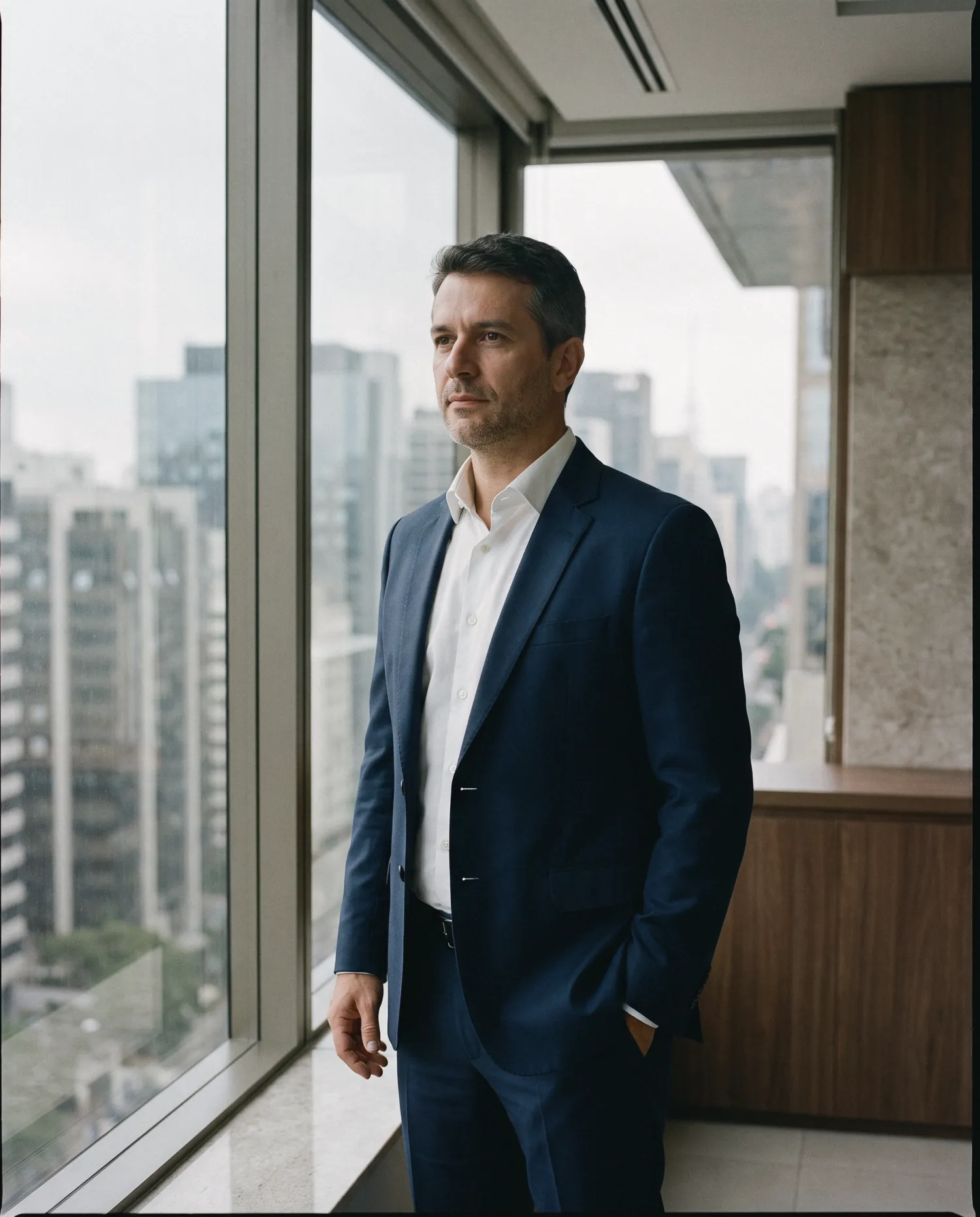 Executivo de terno azul-marinho em escritório alto com vista para os edifícios de São Paulo